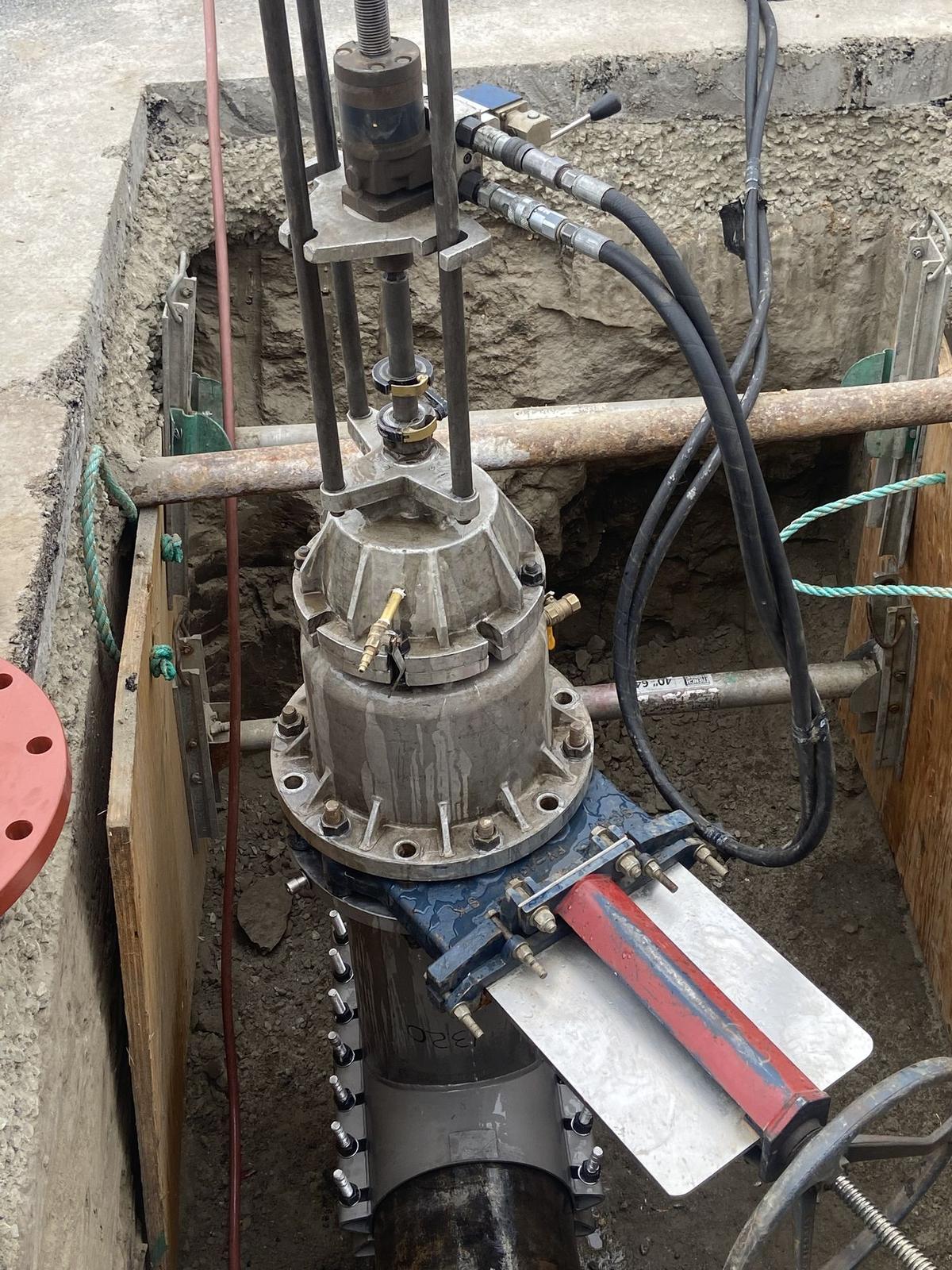 Close view of a tapping machine, hoses, and valve body clamped to a water main.