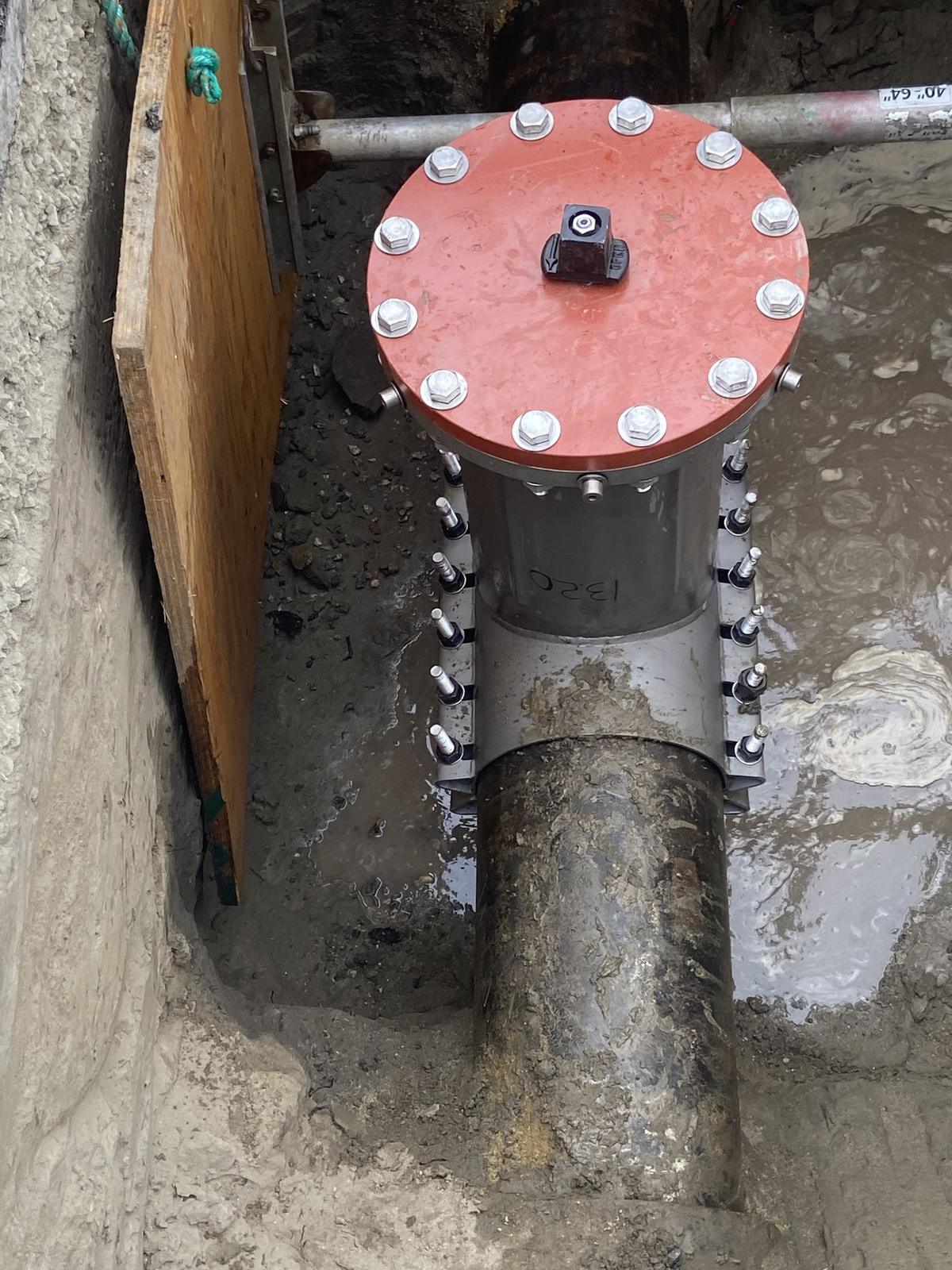 Insertion valve clamped to a water main, red cover and operating nut bolted on.